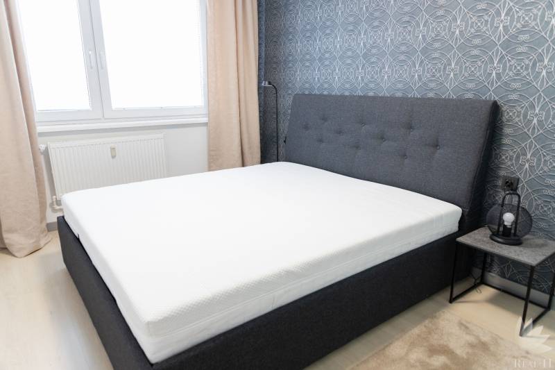 Schlafzimmer mit grauem Bett, gemusterten Tapeten und Nachttisch.