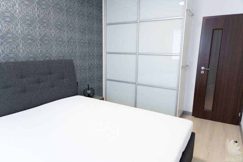 Schlafzimmer in einer 4-Zimmer-Wohnung mit gepolstertem Bett, Tapete und Einbauschrank.