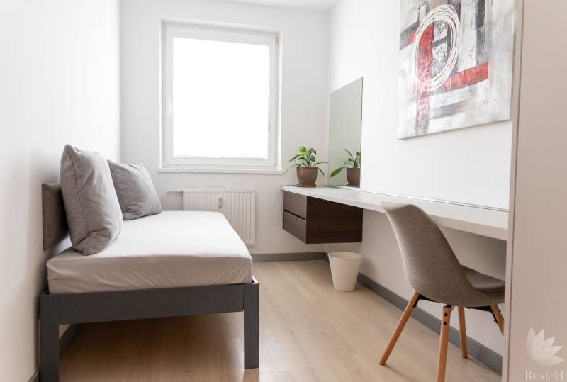 Ein Zimmer in einer 4-Zimmer-Wohnung mit einem Bett, einem Tisch und einem Boden in Holzoptik.