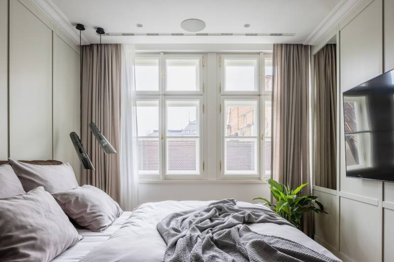 Schlafzimmer in einer 4-Zimmer-Wohnung mit großen Fenstern, Fernseher und neutralen Farben.