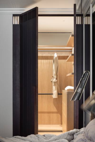 Ein Kleiderschrank mit heller Verkleidung, Kleiderbügel und Beleuchtung in einer 4-Zimmer-Wohnung.