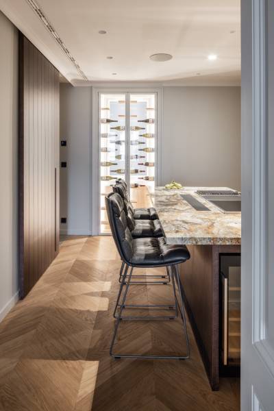 Küche in einer 4-Zimmer-Wohnung mit Bartresen, Stühlen und Boden mit Holzdekor.