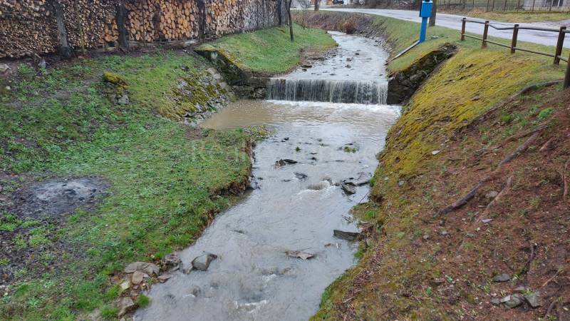 Ein Bach, der durch die Erholungsgebiete in Púchov fließt, mit Holz, das am Rand gelagert ist.
