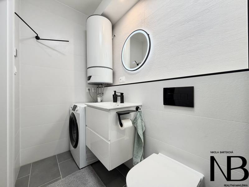 Badezimmer in einer Einzimmerwohnung mit Waschmaschine, Boiler und Spiegel in einem runden Rahmen.