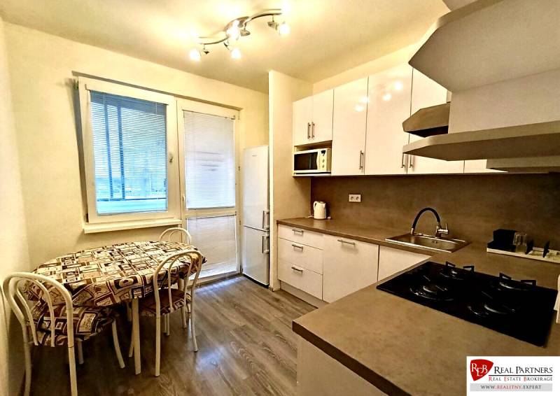 Küche in einer 4-Zimmer-Wohnung mit Holzboden, weißen Schränken und Essecke.
