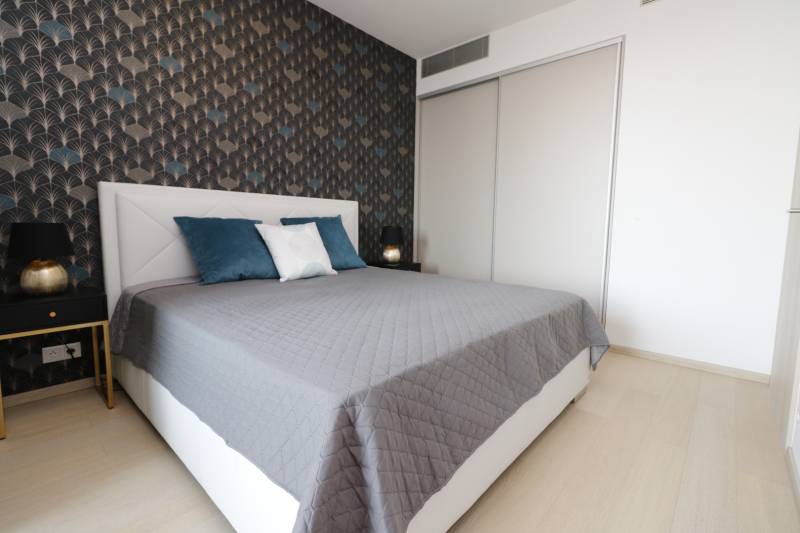 Schlafzimmer mit Bett, gemusterte Wand, Boden mit Holzdekor, 2-Zimmer-Wohnung.