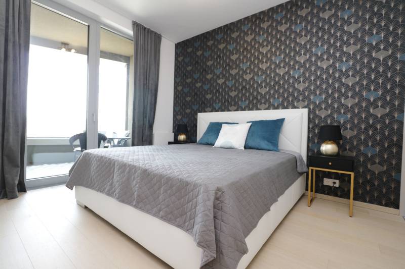 Schlafzimmer mit Bett, Tapete und Zugang zum Balkon in einer 2-Zimmer-Wohnung.