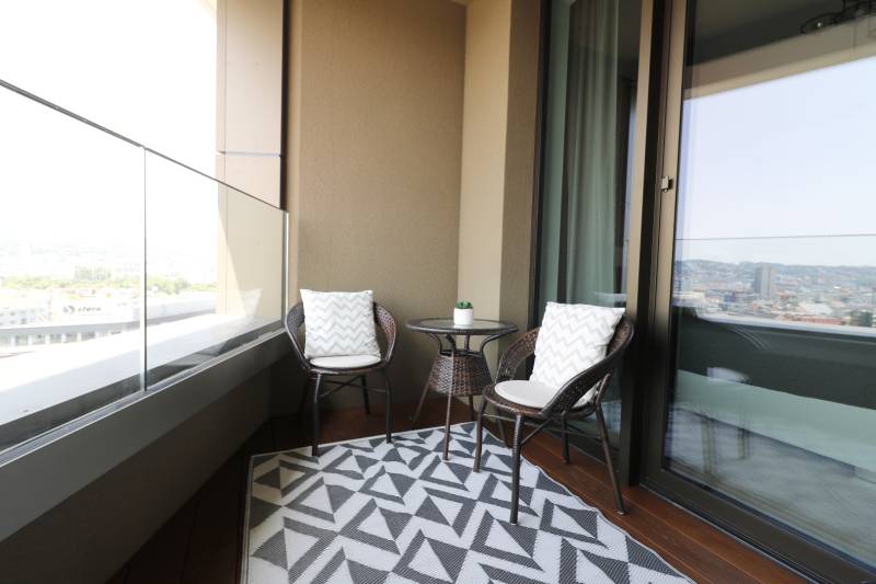 Balkon in einer 2-Zimmer-Wohnung mit Rattanmöbeln und Blick auf die Stadt.