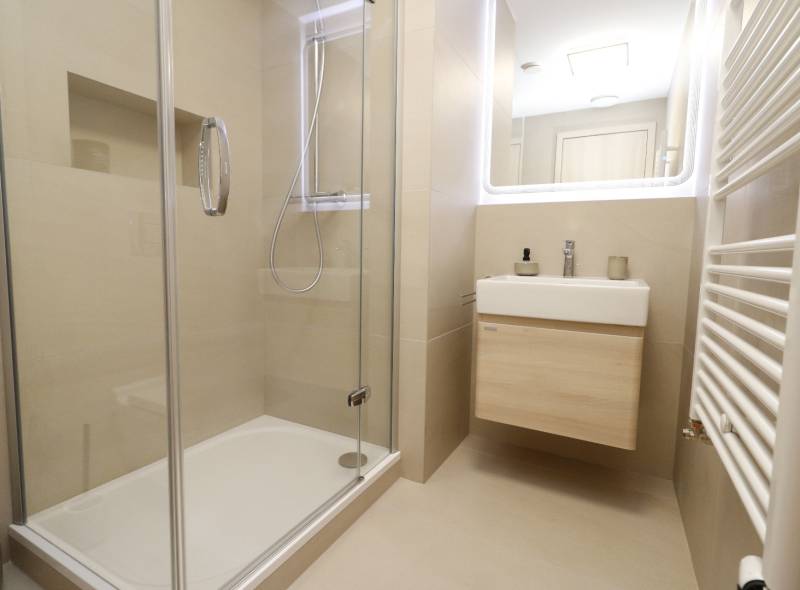 Badezimmer mit verglaster Duschkabine und hellem Waschbecken in einer 2-Zimmer-Wohnung.
