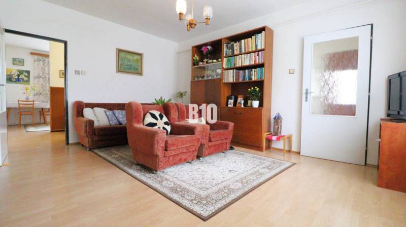 Wohnzimmer eines Einfamilienhauses mit Sofa, Sesseln und Bücherregal auf einem Boden mit Holzdekor.