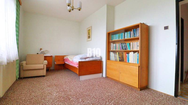 Ein Zimmer in einem Einfamilienhaus mit einem Bett, einem Bücherregal und einem Sessel auf einem Teppich.