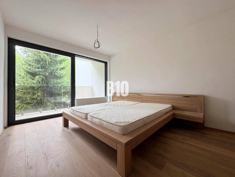 Schlafzimmer in einer 2-Zimmer-Wohnung mit Holzboden und einem großen Fenster zur Terrasse.