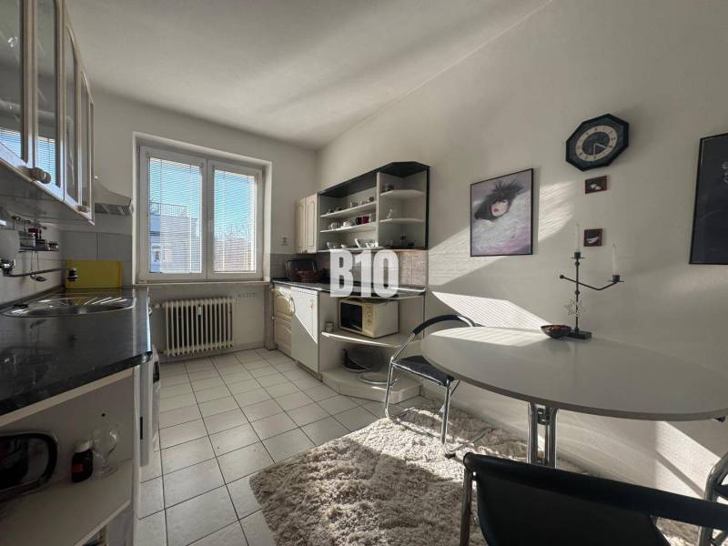 Küche in einer 2-Zimmer-Wohnung mit weißen Schränken, Fenster und Esstisch.
