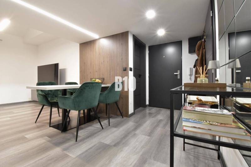 Innenraum einer 4-Zimmer-Wohnung mit Holzboden, Esstisch und grünen Stühlen.