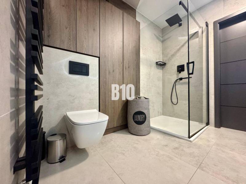 Badezimmer in einer 4-Zimmer-Wohnung mit WC, Dusche und Boden mit Holzdekor.