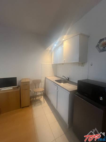 Küchenecke in einem Einzimmerapartment mit Mikrowelle, Kühlschrank und Stuhl.