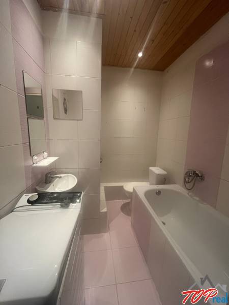 Badezimmer in einem Studio-Apartment mit Badewanne, Waschmaschine, Waschbecken und Toilette.