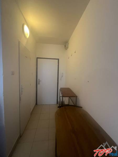 Ein schmaler Flur in einem Einzimmerapartment mit einfacher Einrichtung und weißen Wänden.