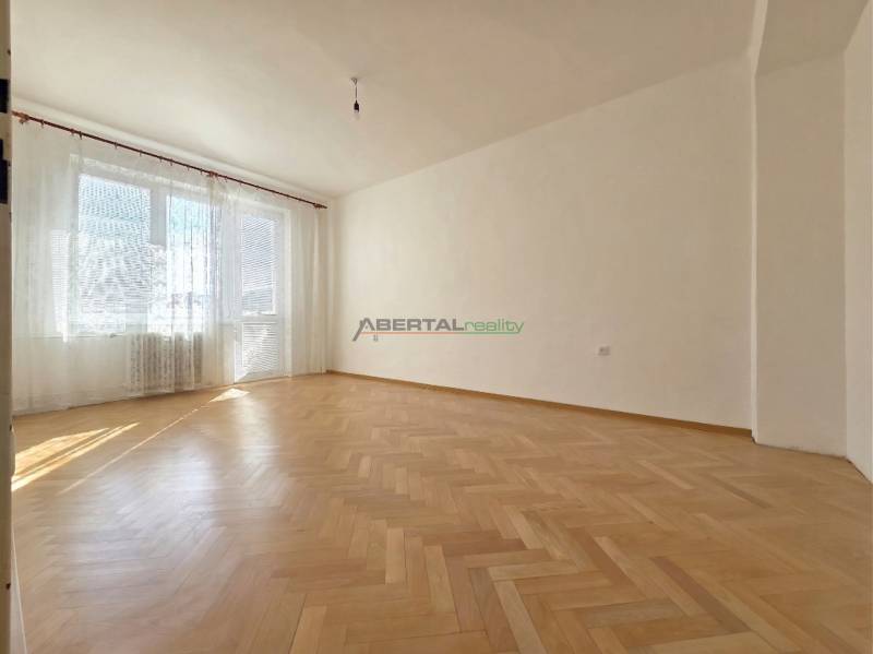 Ein geräumiges Zimmer mit großen Fenstern und einem Boden in Holzoptik in einer 3-Zimmer-Wohnung.