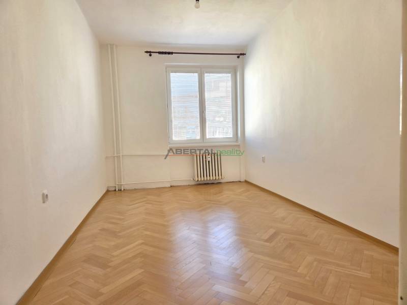 Ein leerer Raum mit Holzboden in einer 3-Zimmer-Wohnung, helle Wände, Heizkörper.