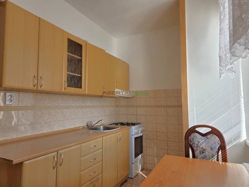 Küche mit hellen Möbeln, Herd und Tisch in einer 3-Zimmer-Wohnung.