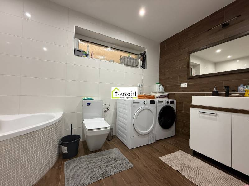 Badezimmer in einem Einfamilienhaus mit Badewanne, Waschmaschine, Trockner und Boden mit Holzdekor.