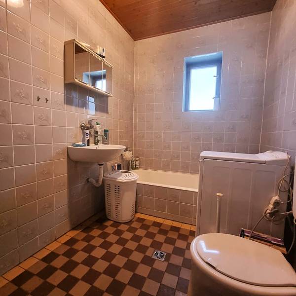 Badezimmer in einem Einfamilienhaus mit Badewanne, Waschbecken und Waschmaschine, Fliesen im Schachbrettmuster.