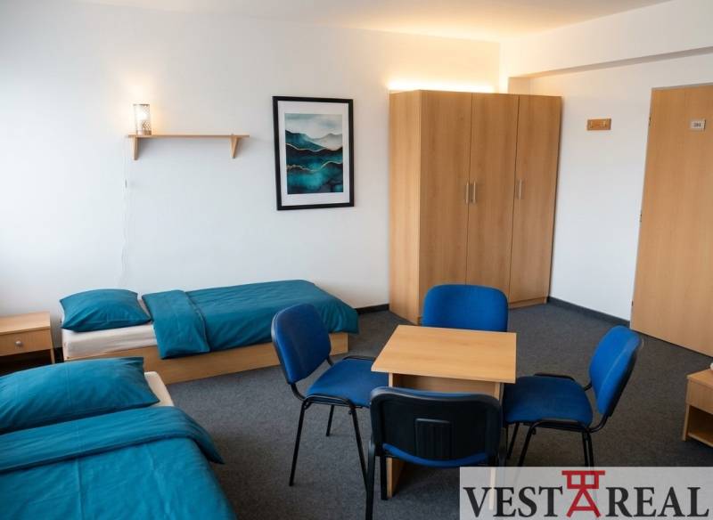 Ein Zimmer mit zwei Betten, blauer Bettwäsche, einem Schrank, einem Tisch und vier Stühlen.