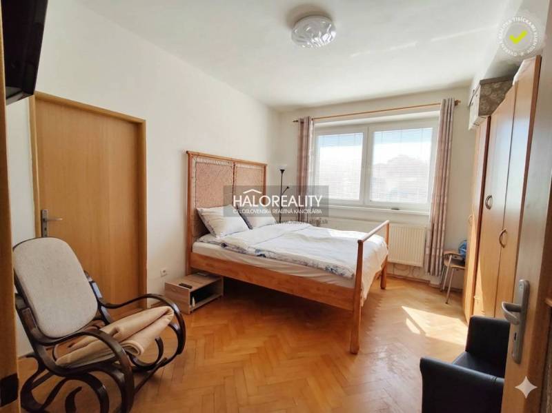 Ein Zimmer in einer 3-Zimmer-Wohnung mit einem Bett, einem Tisch, einem Boden in Holzoptik und gelben Wänden.