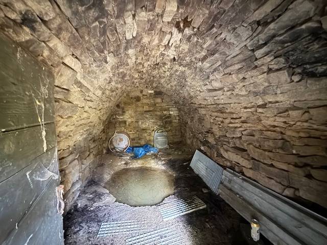 Steinkeller der Hütte mit Gewölbedecke und Metallelementen.