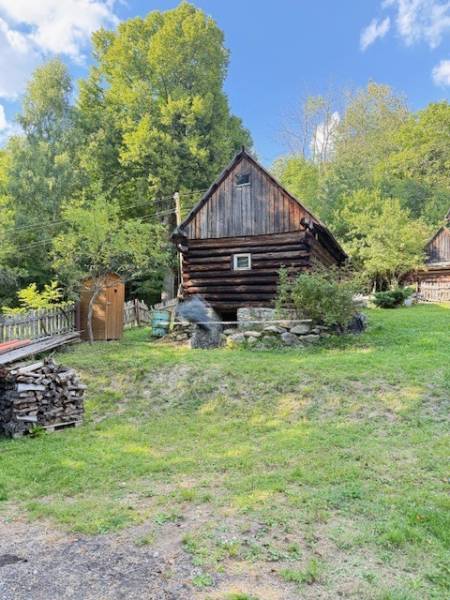 Eine Holzhütte in Horná Mariková, umgeben von Grün und Holzstapeln.