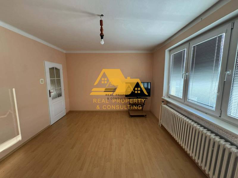 Ein Zimmer in einem Einfamilienhaus mit weißen Wänden, einem Boden in Holzoptik und einem Fenster mit Jalousien.