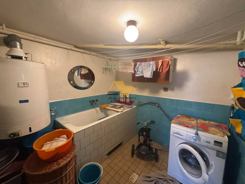 Ein Badezimmer in einem Einfamilienhaus mit einer Badewanne, einer Waschmaschine und einem Boiler, blaue Fliesen.