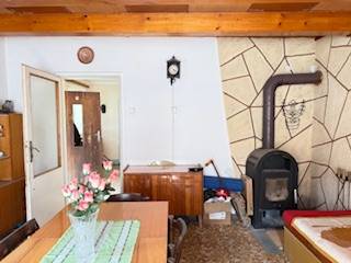 Innenraum eines Einfamilienhauses mit Kachelherd, Holzbalkendecke und Esstisch mit Blumen.