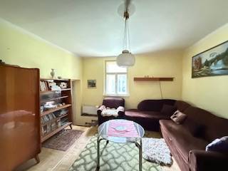 Wohnzimmer mit Teppichen, Büchern, braunem Sofa und Holzboden in einem Einfamilienhaus.