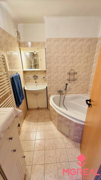Das Badezimmer einer 3-Zimmer-Wohnung mit Badewanne, Waschbecken und beigen Fliesen.