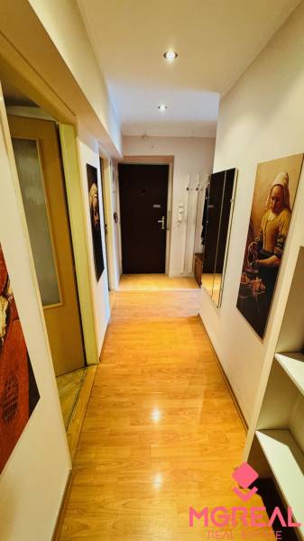 Ein enger Flur mit Holzboden in einer 3-Zimmer-Wohnung, mit Bildern und einem Spiegel.