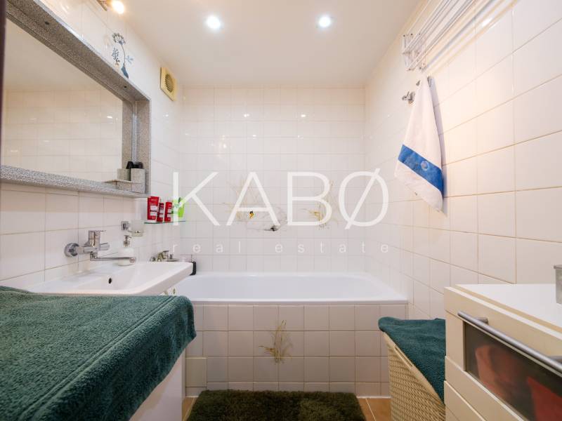 Badezimmer in einer 3-Zimmer-Wohnung mit Badewanne, Waschbecken, weißen Fliesen und grünem Teppich.