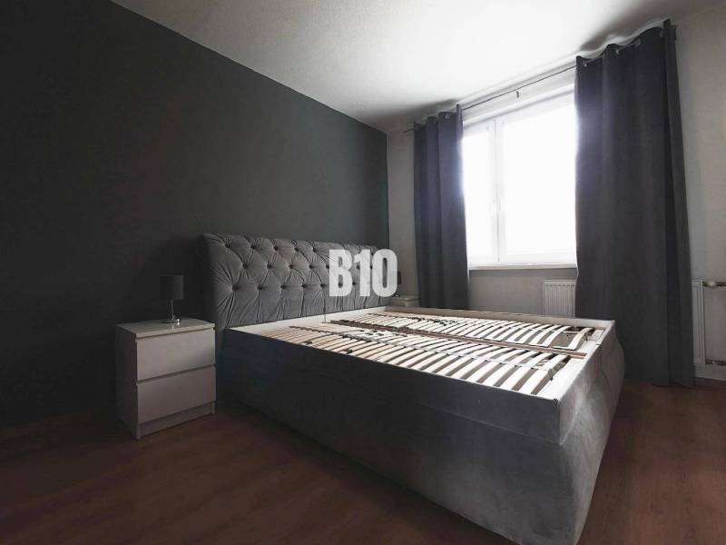 Schlafzimmer mit einem dunkelgrauen Bett, einem Nachttisch und einem Boden mit Holzdekor in einer 3-Zimmer-Wohnung.