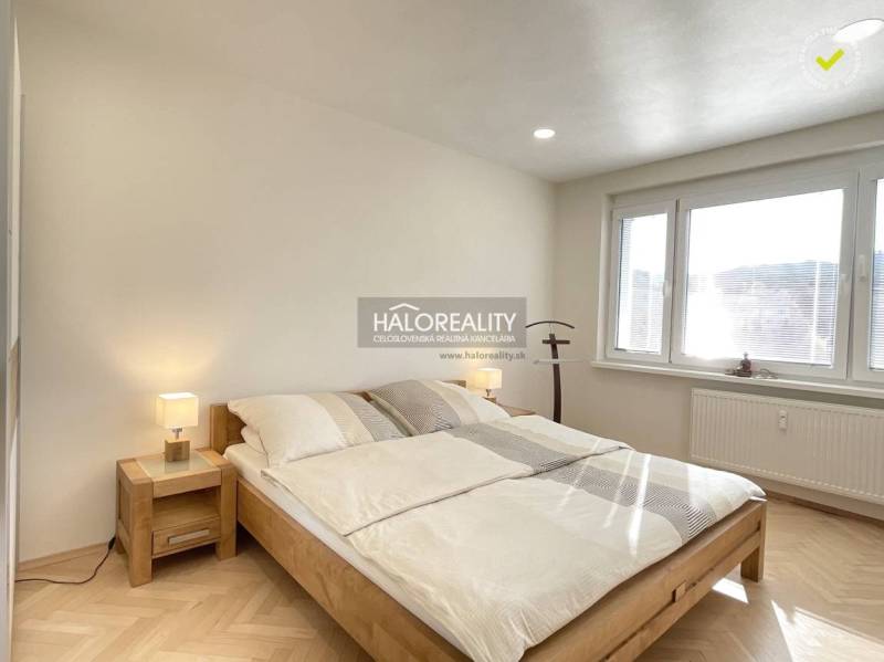 Helles Schlafzimmer in einer Einzimmerwohnung mit Holzboden und großem Fenster.