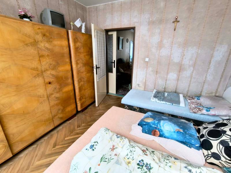 Schlafzimmer in einer 3-Zimmer-Wohnung mit einem großen Holzkleiderschrank und einem Boden mit Holzdekor.