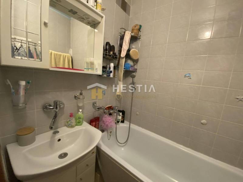Badezimmer mit Dusche und Waschbecken in einer 2-Zimmer-Wohnung mit weißen Fliesen.
