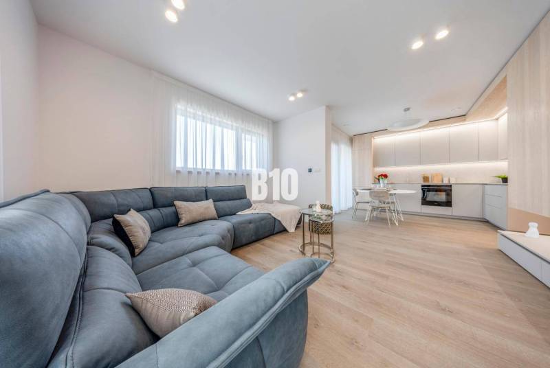 Wohnzimmer mit großer Couch und Küchenzeile, Boden mit Holzdekor.