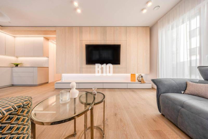 Wohnzimmer in einer 3-Zimmer-Wohnung mit Holzboden und einem Fernseher an der Wand.