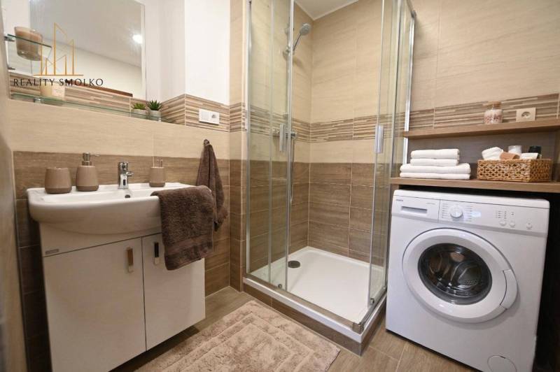 Badezimmer in einer 2-Zimmer-Wohnung mit Waschmaschine und Duschkabine, Boden mit Holzdekor.