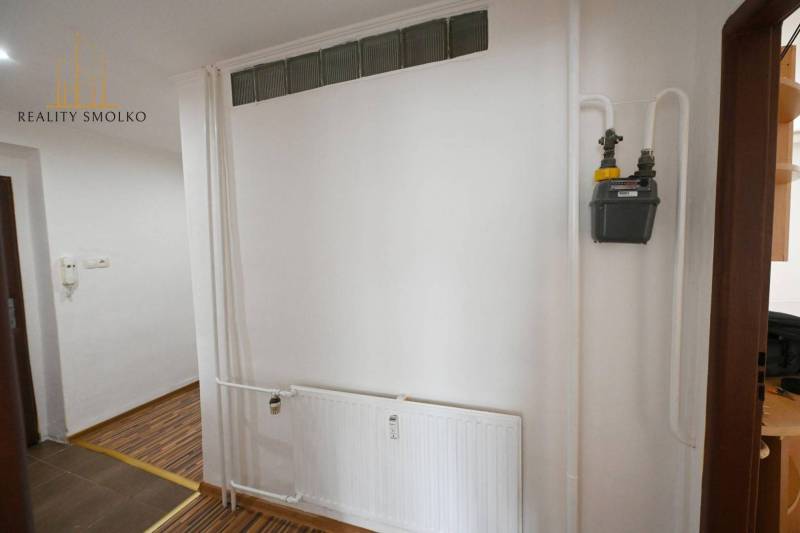 Ein Interieur mit weißer Wand, Heizkörper und Boden mit Holzdekor in einer 2-Zimmer-Wohnung.