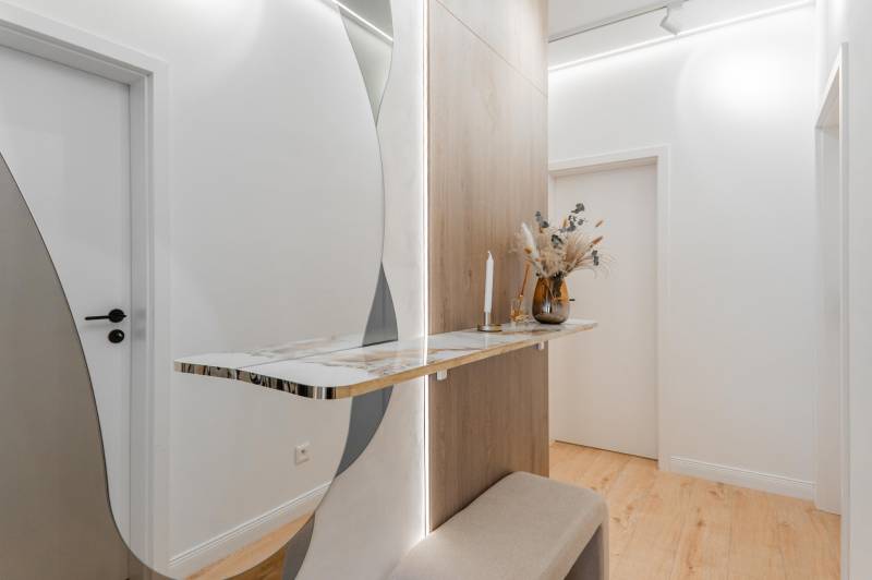 Flur in einer 3-Zimmer-Wohnung mit einem minimalistischen Tisch, einem Spiegel und einem Boden mit Holzdekor.