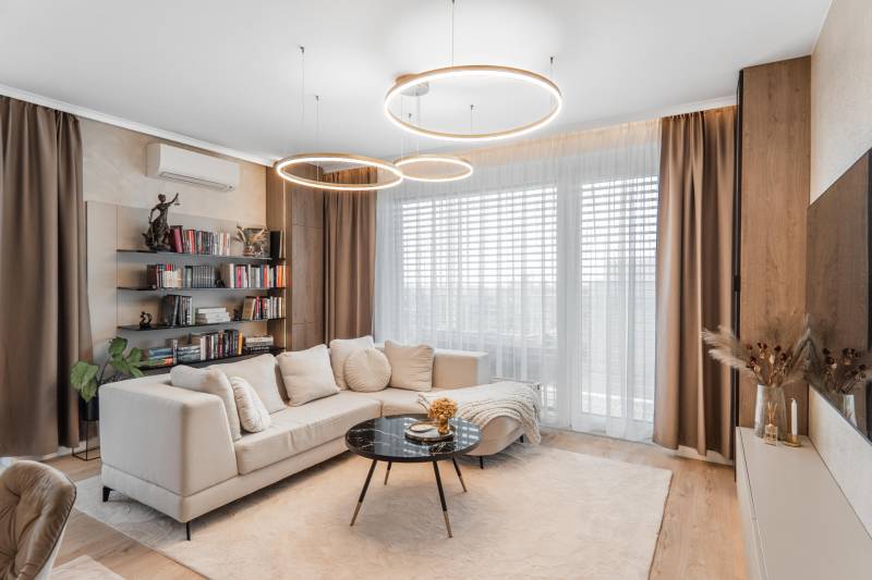 Wohnzimmer mit Holzboden in einer 3-Zimmer-Wohnung, bequeme Couch, Bücherregal.