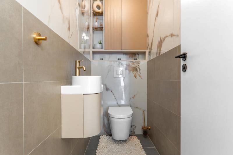 Toilette mit Waschbecken, goldener Wasserhahn und Fliesen mit Marmormuster in einer 3-Zimmer-Wohnung.
