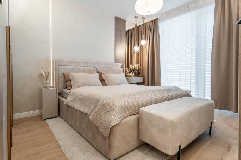 Helles Schlafzimmer mit bequemem Bett, beigefarbenen Vorhängen und Holzbodenoptik.